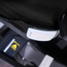 Close-up of the Golden Tech Ally Sport Smart Powerchair seat with ergonomic memory foam, black fabric cover, white plastic button, warning label near the buckle, and a carbon fiber textured surface for enhanced comfort and style.