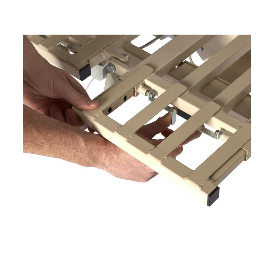 Close-up of hands assembling a Medline Alterra Maxx Long-Term Care Hi/Low Hospital Bed, attaching slats with bolts and nuts. The hands and frame components are shown, highlighting the integrated width and length adjustment features.