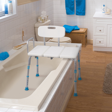 The Drive Aquasense Adjustable Bathtub Transfer Bench, featuring sturdy metal legs, straddles the bathtub edge in a white-tiled bathroom with wood flooring and blue towels, offering added support and convenience for safe bathing.
