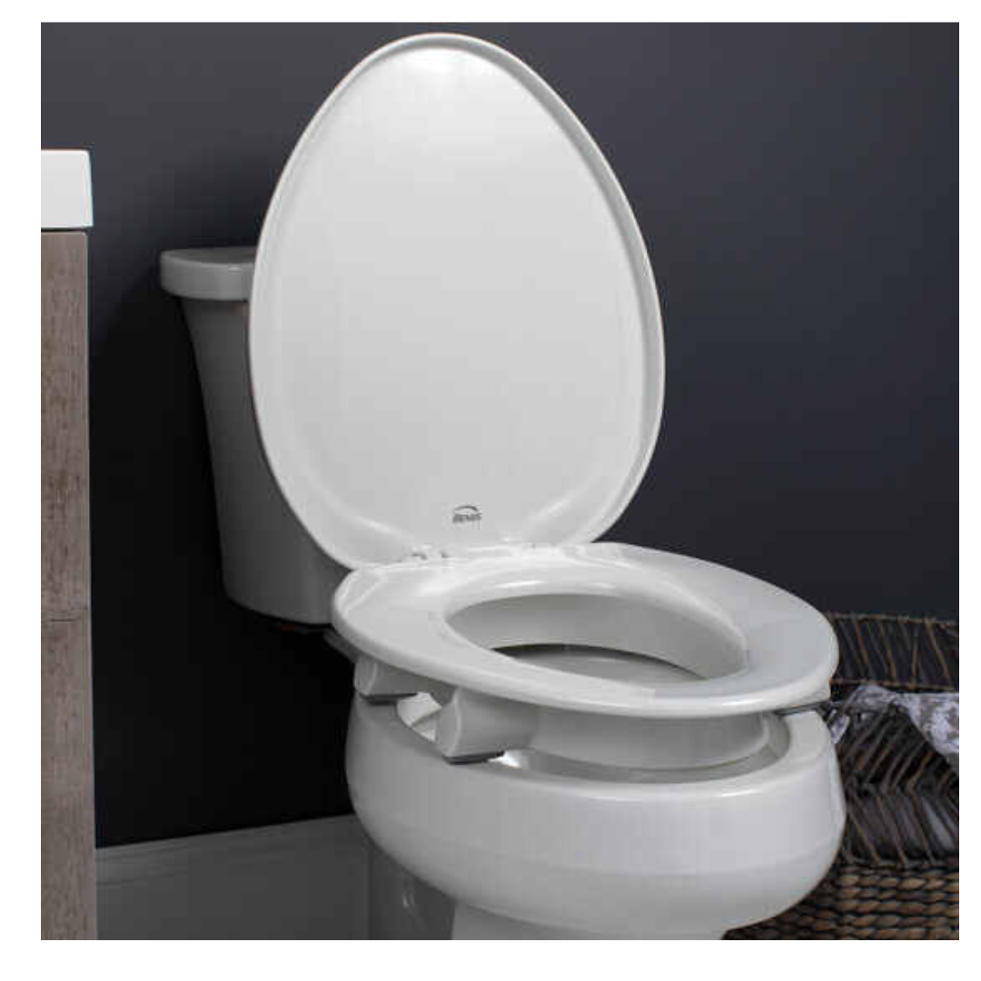 A Bemis Assurance® with Clean·Shield 3 Premium Raised Toilet Seat is shown with a raised lid against a dark gray wall, flanked by wooden decor on the left and a towel basket on the right, and includes a child seat adapter.