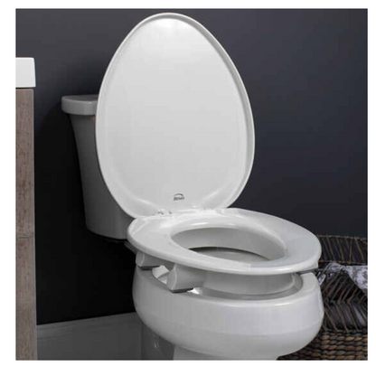 A Bemis Assurance® with Clean·Shield 3 Premium Raised Toilet Seat is shown with a raised lid against a dark gray wall, flanked by wooden decor on the left and a towel basket on the right, and includes a child seat adapter.