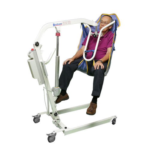 An older adult is comfortably seated in a Bestcare General Purpose Clip Sling With Padded Legs For PL350CT, featuring integrated head support, while being lifted by a white mobile patient lift on wheels. They are relaxed in a purple shirt and black pants against a crisp white background.