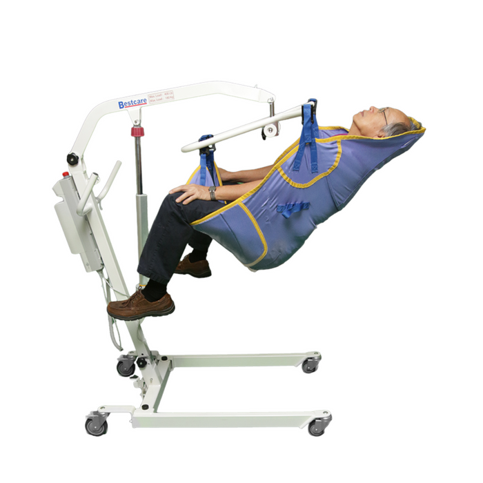 A person reclines in the Bestcare General Purpose Clip Sling with padded legs, fitted to a white portable lift that has an integrated head support and utilizes a hydraulic arm. Padded leg supports and wheels finish the lift; the individual wears black pants and brown shoes.