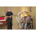 A caregiver uses the Bestcare BestLift PL400EF Compact Foldable Electric Mobile Floor Lift to assist a person in a wheelchair. The room, decorated with paintings and featuring a bed, provides a calm and supportive atmosphere.