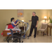 A man in black gently transfers a woman from bed to wheelchair with the Bestcare BestStand® SA Series Sit-to-Stand Patient Lift, offering ergonomic comfort and safety. The room has soft lighting, a wall painting, and a table plant.