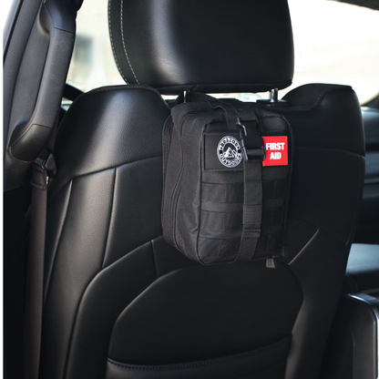 A Brazos First Aid Survival Kit - 250 Pieces is strapped to a black leather car seat headrest. The kit is black and features a red First Aid patch and a round logo patch.