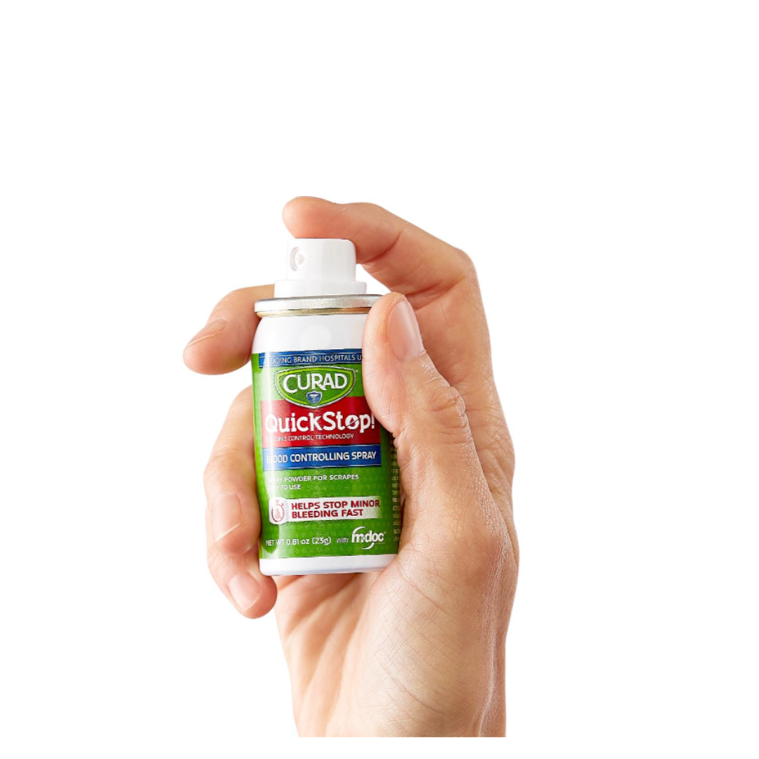 A hand holds a can of CURAD QuickStop! Blood Controlling Spray, pressing the nozzle on the green and white can against a white background, demonstrating its fast bleeding control for trusted first-aid care.