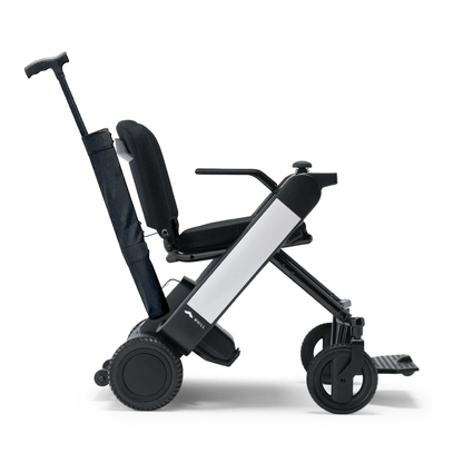 A Cane Holder for the WHILL Model F Powerchair is shown attached to the side of this modern, compact foldable wheelchair, featuring large rear wheels, a slim frame, a collapsible backrest, and an extendable handle for easy transport.