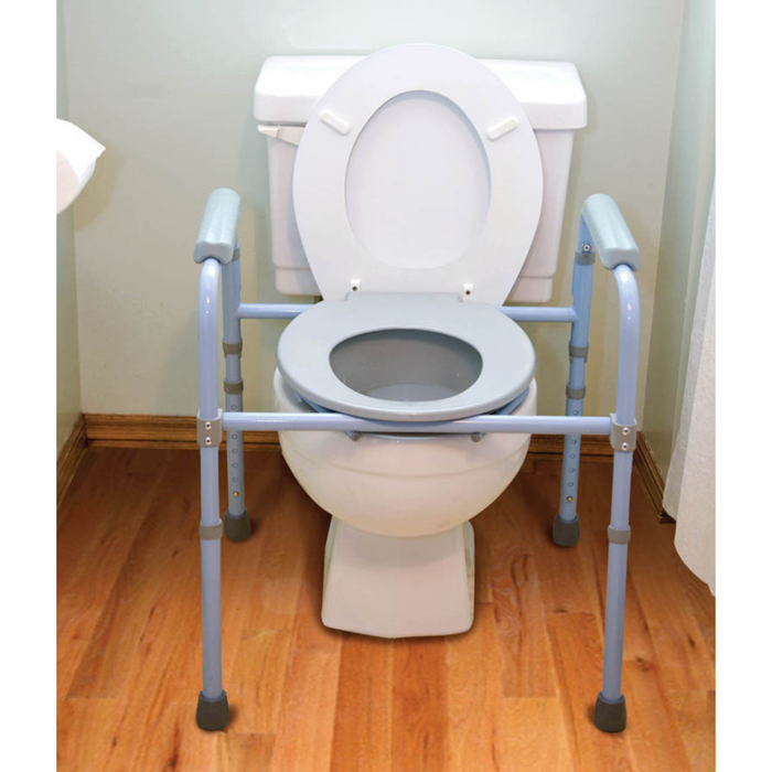 The bathroom showcases the Carex Deluxe Folding Commode with a light blue safety frame for support. Wooden floors complement this setup, while grab bars enhance safety. A white toilet tank adds to the convenience and security provided by this compact, versatile product.