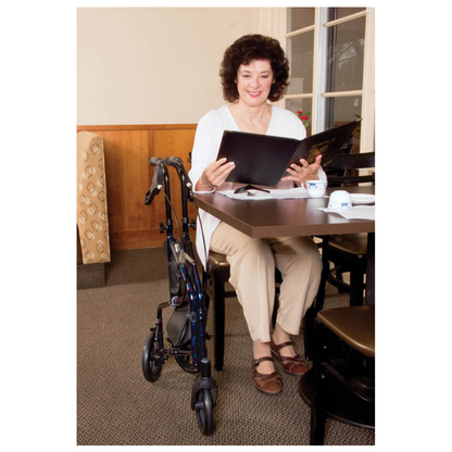 A woman sits at a restaurant table, reading a menu. Her Carex Trio Roller 3-Wheel Walker Rollator is next to her. Smiling, she appears to be deciding what to order.