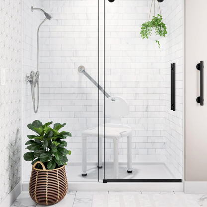 A modern shower with white subway tiles, glass door, wall-mounted showerhead, grab bar, hanging plant, woven basket with green potted plant, and a Carex Bariatric Bath Seat And Shower Chair with Backrest for seniors.