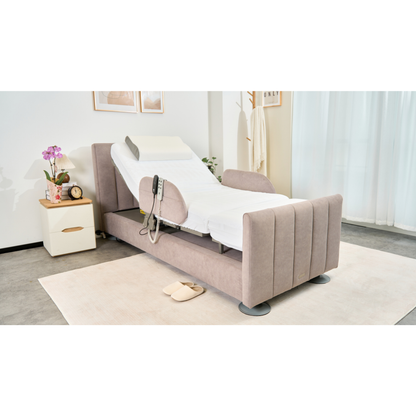 The Charme Starsleep Orin Rotating Full Electric Lift Assist Bed with Heat & Massage, in light beige upholstery, is partially elevated in a bright bedroom with slippers, a nightstand holding a clock and plant, and a robe hanging nearby.
