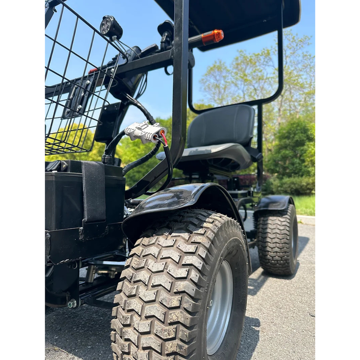 Close-up of a black Green Transporter Cheeta Ninja All-Terrain HD Scooter Golf Cart with large rugged tires on pavement. A front basket is visible, with green trees and a clear blue sky in the background.