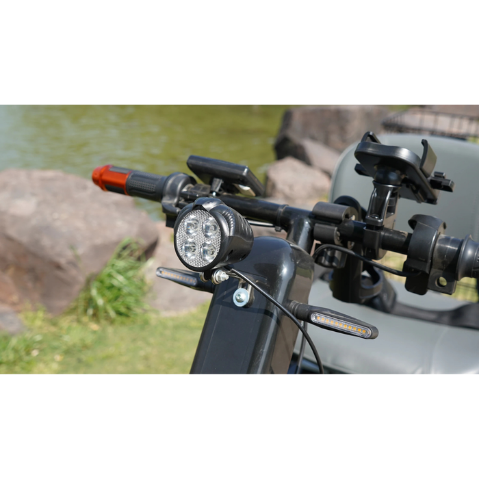 Close-up of the Green Transporter Cheeta Ninja All-Terrain HD Scooter Golf Cart’s handlebars with LED headlight, phone holder, and controls—highlighting off-road capability near rocks and a grassy pond for ultimate outdoor adventure.