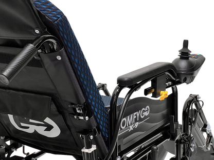 Close-up of the ComfyGo X-9 electric wheelchair featuring a blue mesh seat and joystick control on the armrest. This advanced mobility solution includes a storage pouch with logo and model name OMFYGO X-9 on the side.