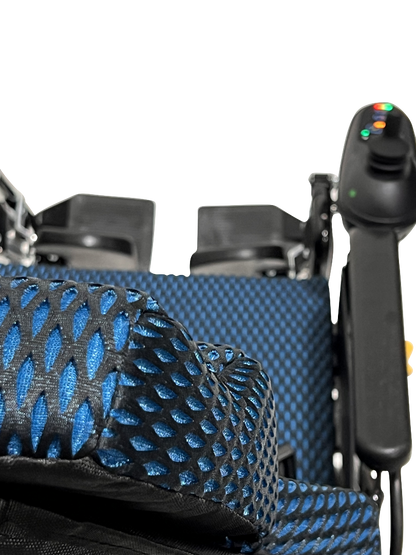 A close-up of the blue and black mesh seat on the ComfyGo X-9 Remote Controlled Powerchair highlights its sleek design. The right armrests control panel with colored buttons stands out, similar to a remote-controlled wheelchair, against a neutral background.