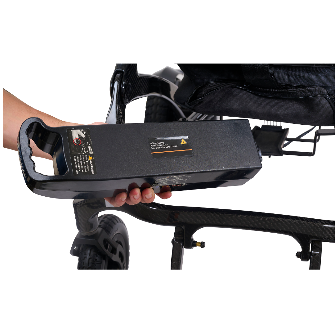 A hand removes a rectangular black Golden Technologies GP302 Cricket accessory battery pack from beneath the seat of a recumbent tricycle.