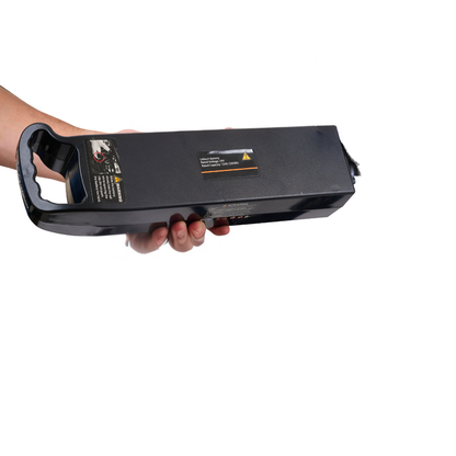 A hand holding a black rectangular Golden Technologies GP302 Cricket accessory battery with a handle and warning labels, isolated on a white background.