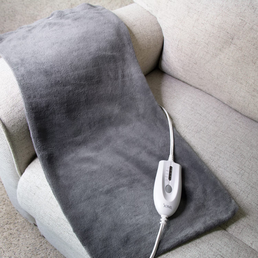 The DMI Dry and Moist Heat Electric Heating Pad, featuring a white electronic controller, is draped over a light-colored sofa armrest, ready to deliver soothing pain relief.