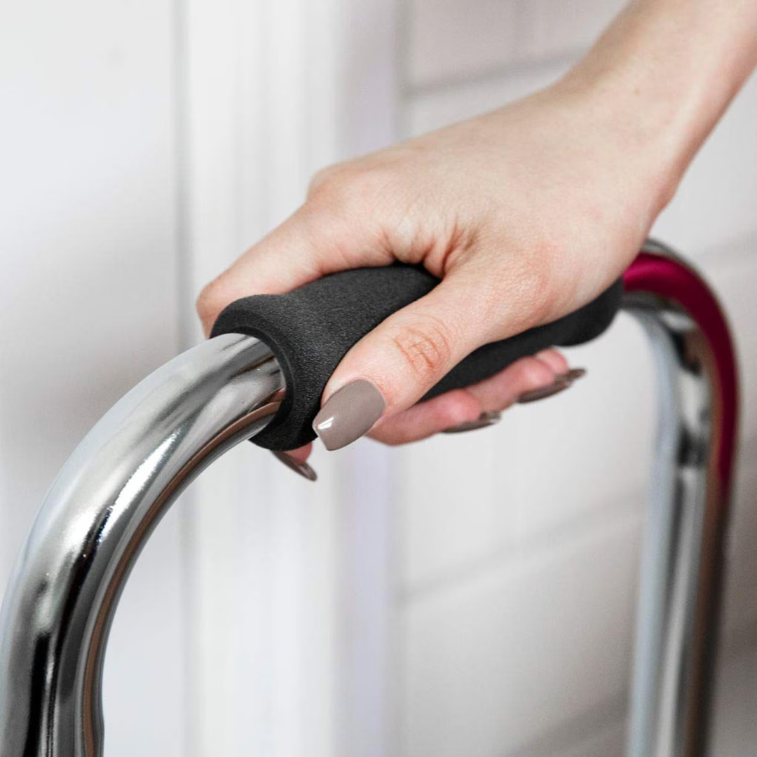 A close-up of a person's manicured hand gripping the foam handle of the DMI Step Stool and Non Skid Rubber Platform, designed for safe mobility assistance, against a white tiled background.