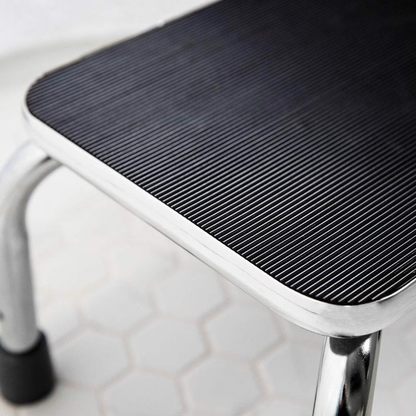 The DMI Step Stool and Non Skid Rubber Platform features a rectangular black ribbed surface and chrome legs, placed on white hexagon tiles—ideal for safe mobility assistance at home.