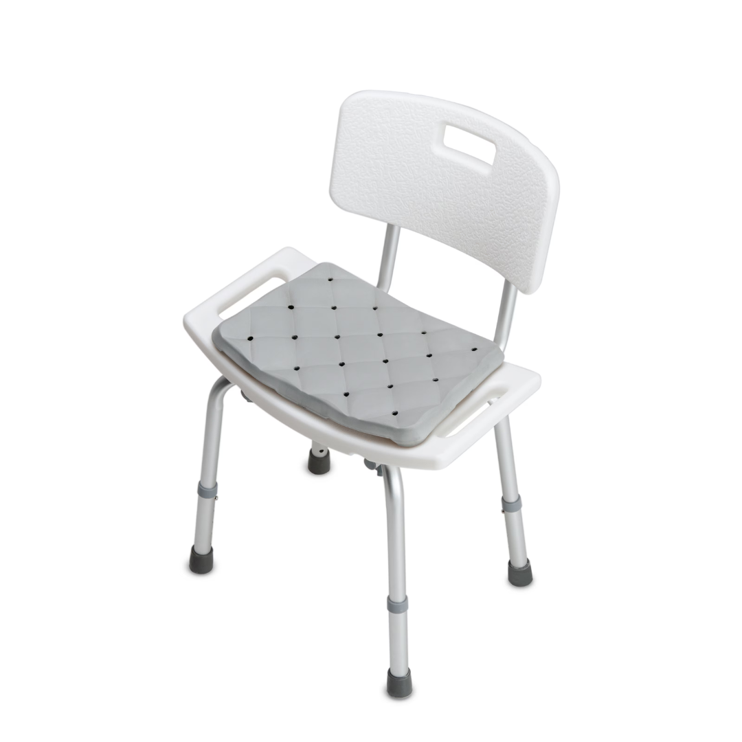 A white shower chair with backrest, armrests, and adjustable legs includes the DMI Waterproof Foam Bath Seat Cushion in gray for extra comfort and support. The bath seat is displayed on a plain white background.