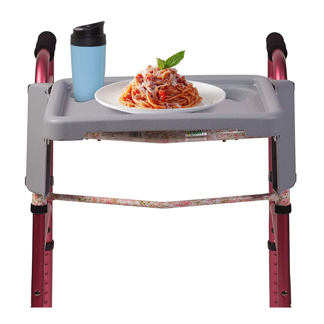 The DMI® Folding Walker Tray with Cup Holders fits on a pink walker, shown holding a blue travel cup and a plate of spaghetti with tomato sauce, cheese, and basil—a practical accessory for seniors.