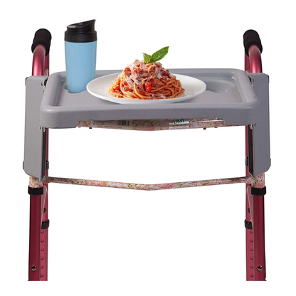 The DMI® Folding Walker Tray with Cup Holders fits on a pink walker, shown holding a blue travel cup and a plate of spaghetti with tomato sauce, cheese, and basil—a practical accessory for seniors.