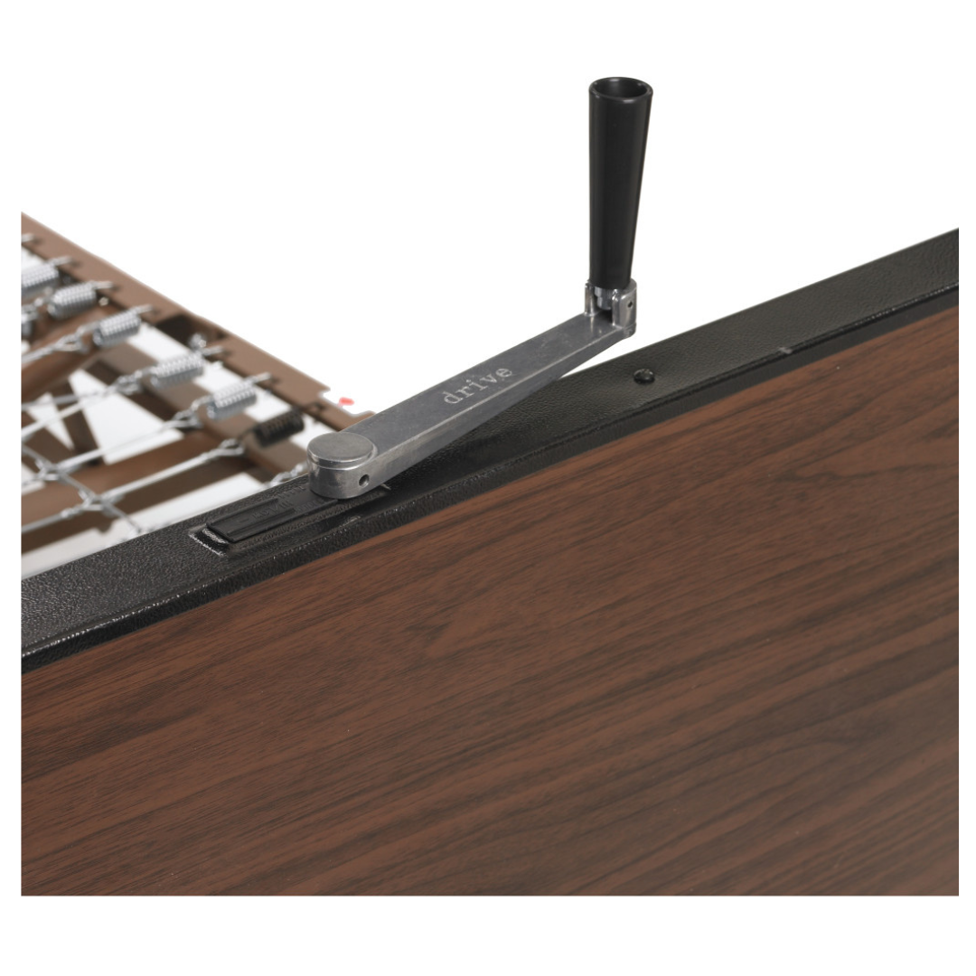 A close-up of the Drive Delta® Ultra-Light 1000 Bariatric Full-Electric Low Bed's crank handle, attached to a wood-grain footboard for bed height or position adjustment. "drive" is visible on the metal crank.