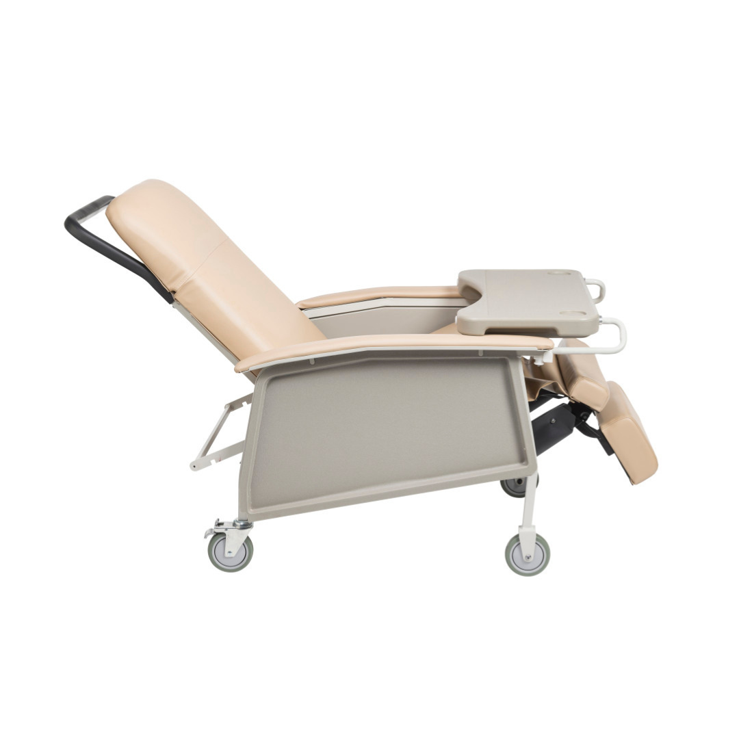 The Drive 3-Position Geri-Chair Recliner with Wheels is shown in side profile, featuring a beige padded seat and backrest, an attached tray table on one armrest, footrest extended, and four caster wheels for easy mobility.