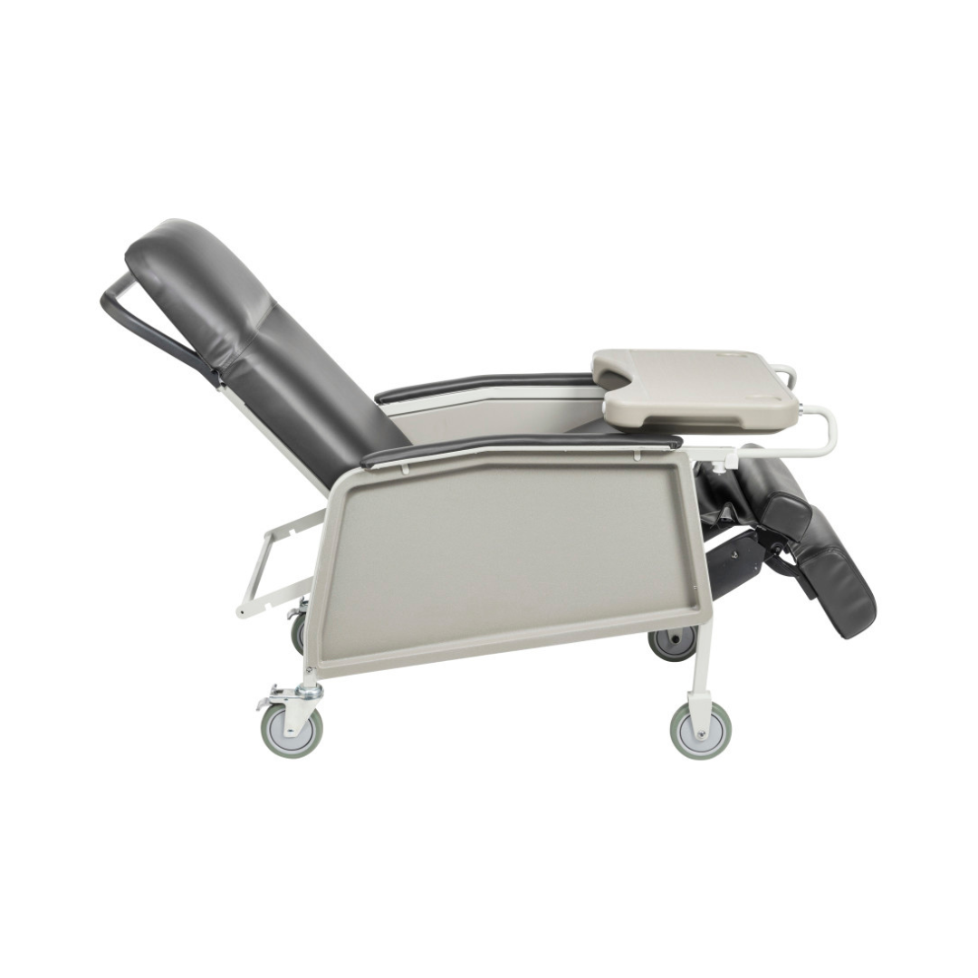 The Drive 3-Position Geri-Chair Recliner with Wheels in black and gray is shown reclined, featuring a padded seat, adjustable leg rest, and a foldable tray on one armrest for enhanced patient comfort.