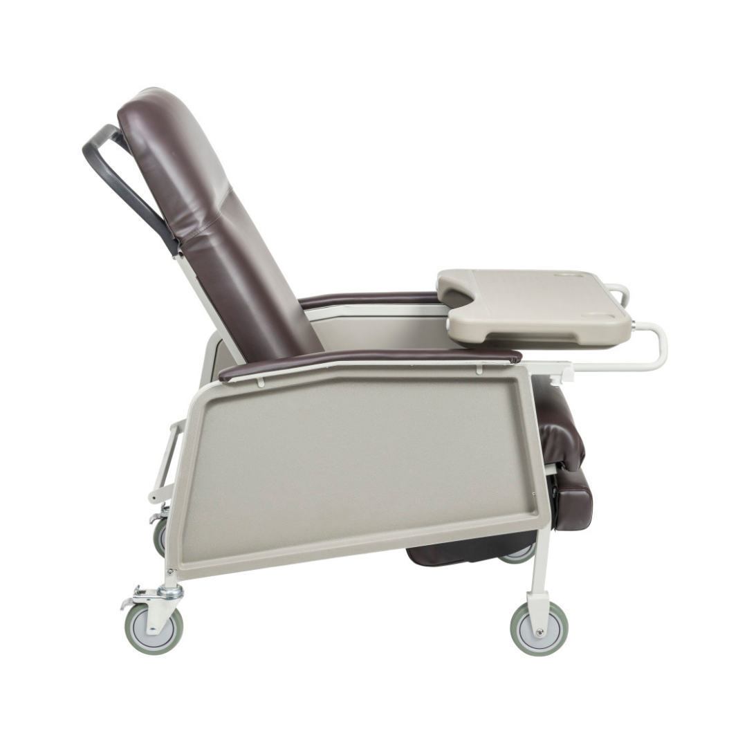 The Drive 3-Position Geri-Chair Recliner with Wheels is shown in brown cushioned upholstery and a light grey frame, featuring an adjustable tray table. Ideal as a patient care chair, it offers comfort, mobility, and convenience.