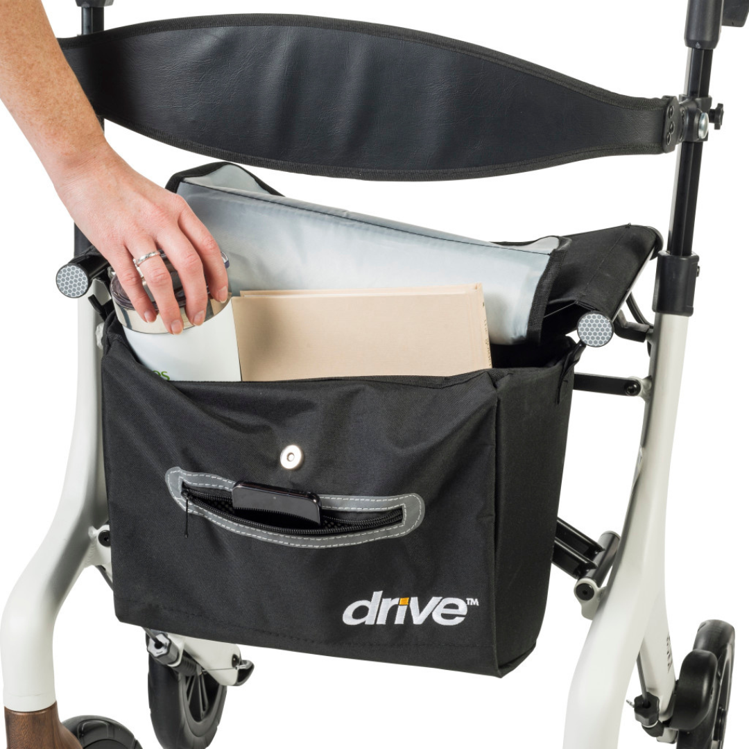 A person places a cup and folder into the black storage bag with button closure, labeled "drive," beneath the seat of the Drive AeroWalk Ultra-Lite Rollator, an ultra-lightweight walker with adjustable handles and backrest.