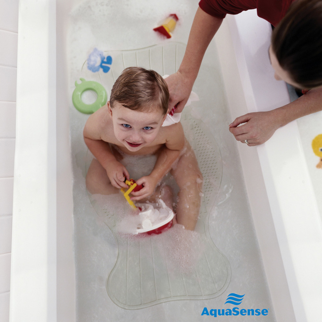 A child plays with a toy boat in the tub while an adult washes their hair. Bath toys float around, and the Drive AquaSense Bath Mat - Contoured Regular Size provides non-slip safety. The AquaSense logo appears in the bottom right corner.