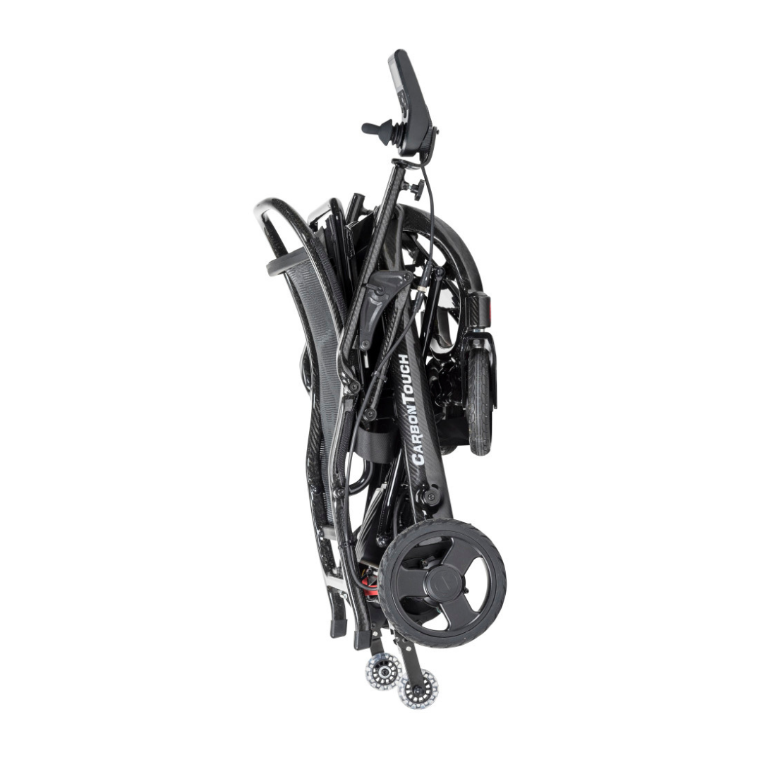 A black lightweight power wheelchair folded upright for transport or storage, with the label CARBON TOUCH visible on the frame and small wheels at the base. This is the innovative Drive CarbonTouch Power Wheelchair, designed for both convenience and portability.