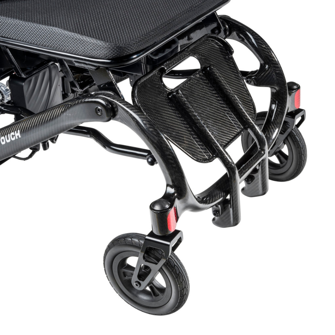 Close-up of the front section of a Drive CarbonTouch Power Wheelchair, displaying the footrest, small front wheels, and part of the seat above.