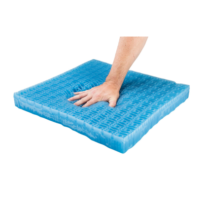 A hand presses down on a blue, grid-patterned Drive DualEase™ Gel Cushion - All Purpose Portable Cushion, creating an indentation to highlight its softness and flexibility. The reversible gel seat cushion is shown against a clean white background.