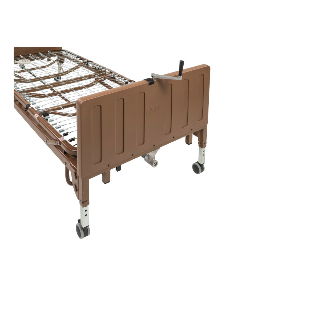 The Drive Full Electric Low Height Homecare Bed, shown from the foot end, is a brown bed frame on wheels with metal springs and a hand crank for height adjustments. No mattress or bedding is included.