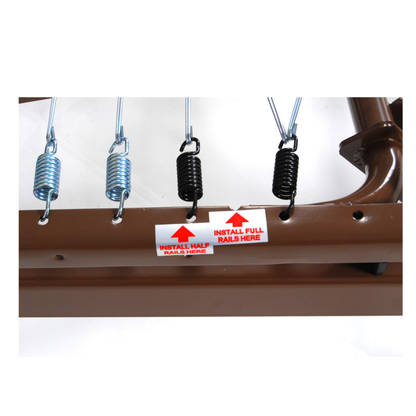 Close-up of a brown metal frame on the Drive Full Electric Low Height Homecare Bed with four attached springs—two silver and two black. Labels read: "INSTALL HALF RAILS HERE" under silver, "INSTALL FULL RAILS HERE" under black.