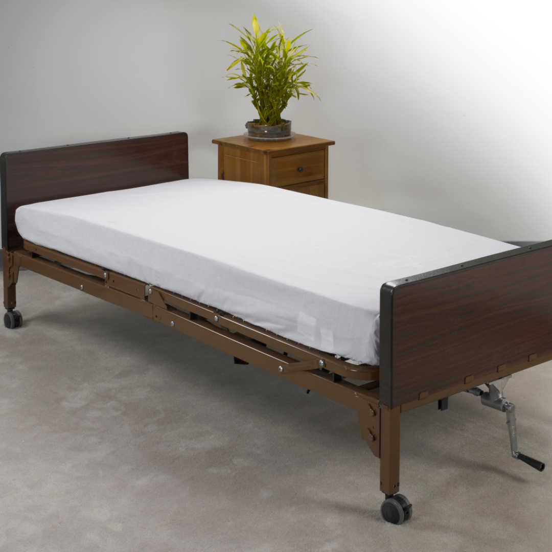 The Drive Hospital Bed Linen Kit is seen on a hospital bed with a brown headboard and footboard on wheels, next to a wooden nightstand with a potted plant, set on a light carpet—perfect for homecare beds.