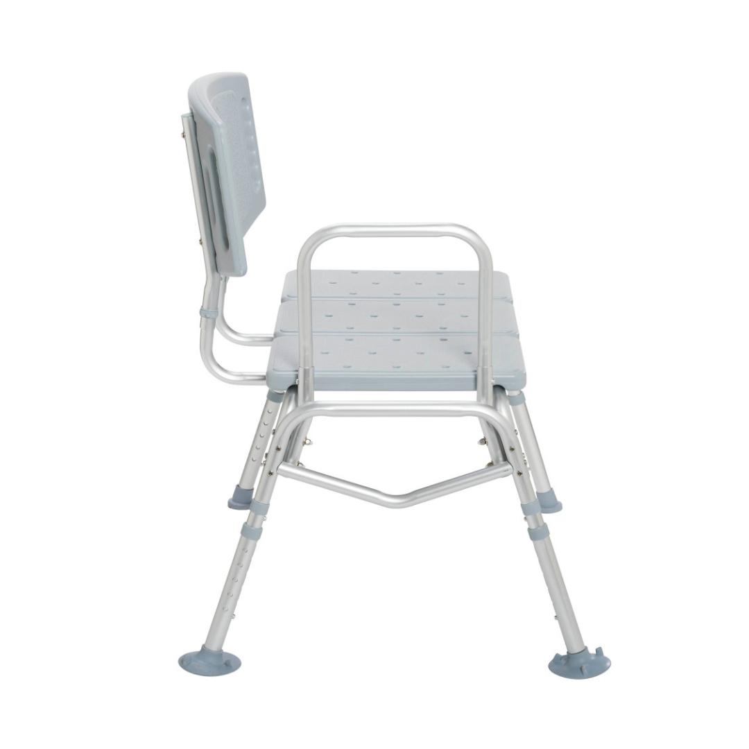 The Drive Bariatric Transfer Bench is a light gray, heavy-duty shower bench with backrest, armrests, and adjustable legs with rubber tips for stability. The seat and back have drainage holes. The bench faces left on a white background.