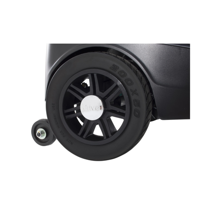 Close-up of a large black wheel with a silver center attached to the Drive Scout Compact 3-Wheel Scooter, with a smaller stabilizing wheel on the left.