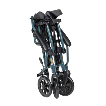 The Drive Travelite Transport Chair—Ultra Compact with rolling travel bag—features black armrests and large black wheels, folded upright on a white background.