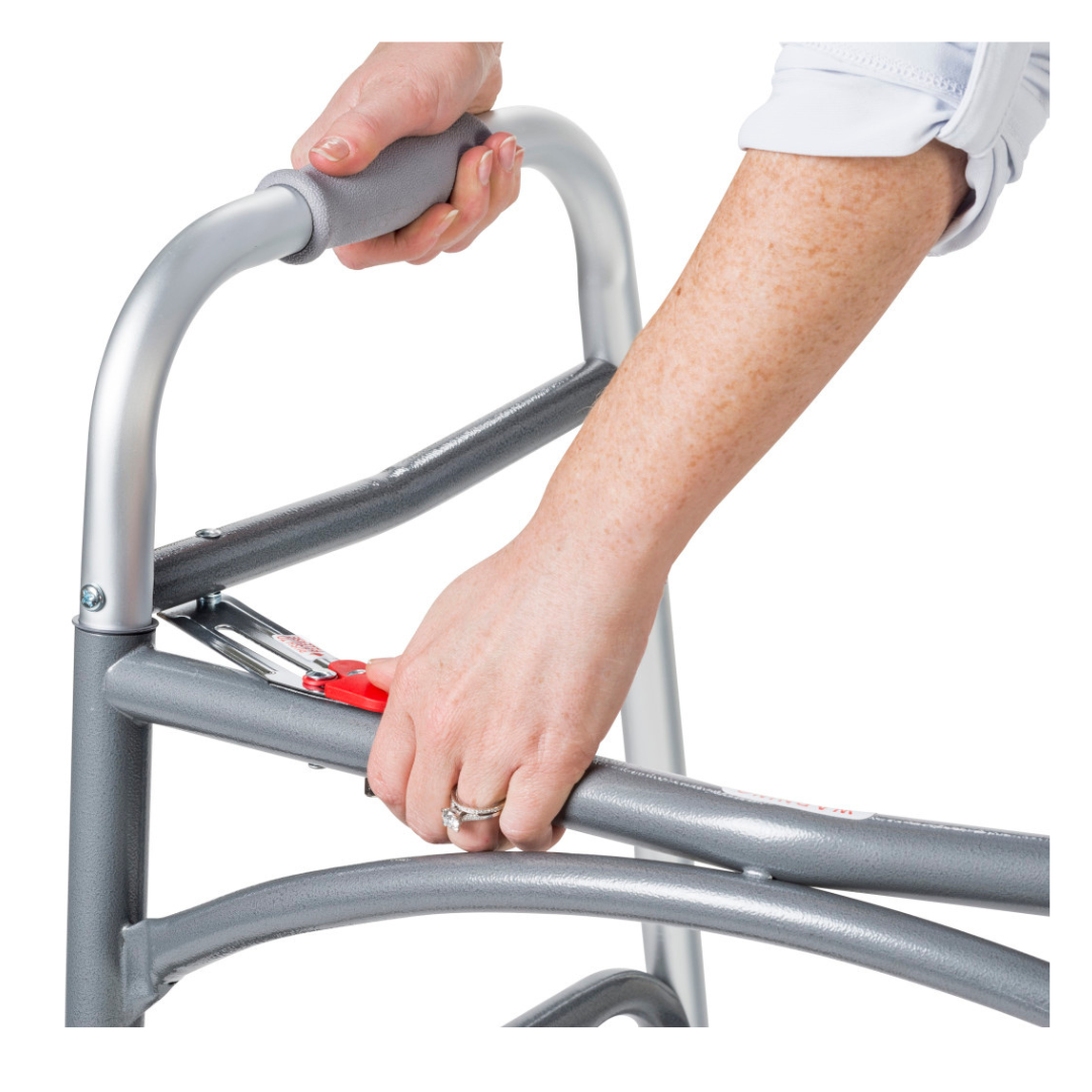 A person in a white shirt adjusts the height of a Drive Bariatric Aluminum Two Button Folding Walker using its red lever button. A ring is visible on their left hand as they handle the sturdy gray walker.