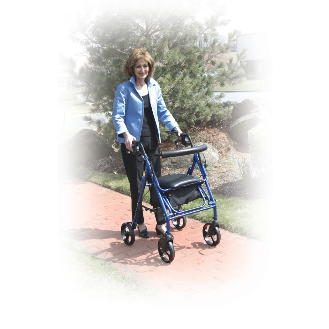 A woman in a blue jacket uses the Drive Hybrid Duet Rollator/Transport Chair on a red brick path outdoors, surrounded by trees and shrubs.