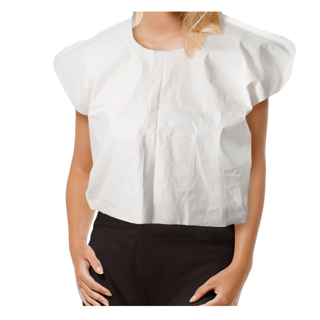 A woman wears a loose-fitting Dynarex Exam Cape with short sleeves, resembling a white blouse, paired with black pants while standing against a white background.