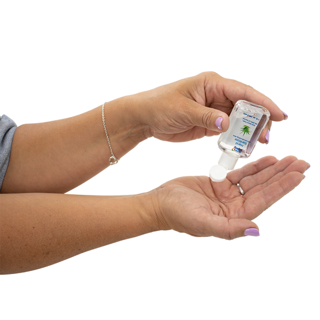 A person with light purple nails and a silver bracelet dispenses Dynarex Hand Sanitizer with Moisturizing Aloe from a small clear bottle onto their open palm against a white background.