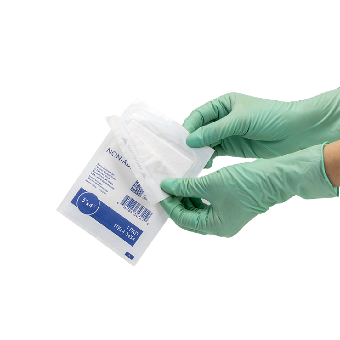 A person in green medical gloves is opening a package of Dynarex Non-Adherent Dressing Pads - Sterile, displaying the white pads partially out of the packaging against a white background for optimal wound protection.