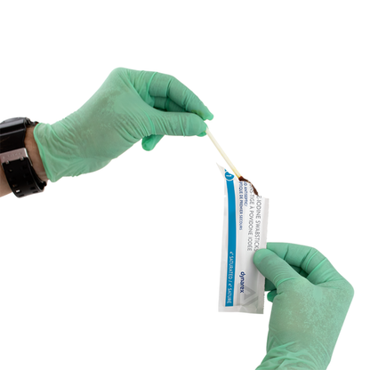 A person in green gloves opens a sterile Dynarex Povidone Iodine Swabsticks package and removes a swabstick with one hand, preparing it for antiseptic skin prep. The background is white.
