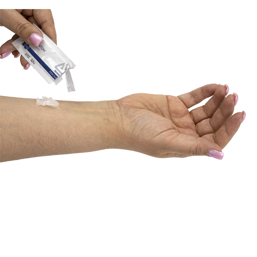 A person with light brown skin and neatly manicured pink nails applies Dynarex White Petrolatum – Petroleum Jelly Skin Protectant from a tube onto their inner forearm using their other hand.